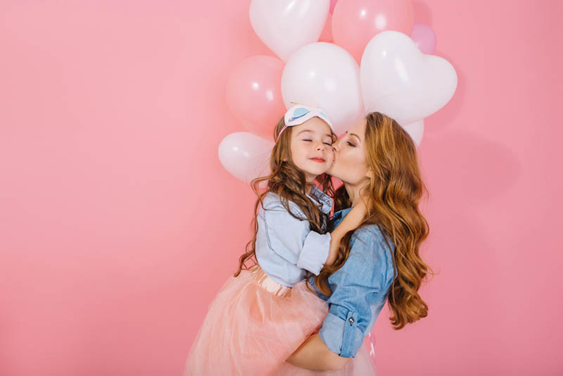 Junge Frau küsst ihre kleine Tochter an ihrem Geburtstag