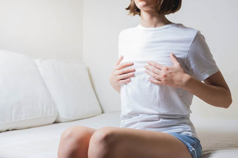 Junge Frau sitzt im Schlafzimmer und hält für schmerzhafte Brust