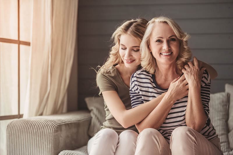 Junge Frau umarmt ihre Mutter auf der Couch zu Hause