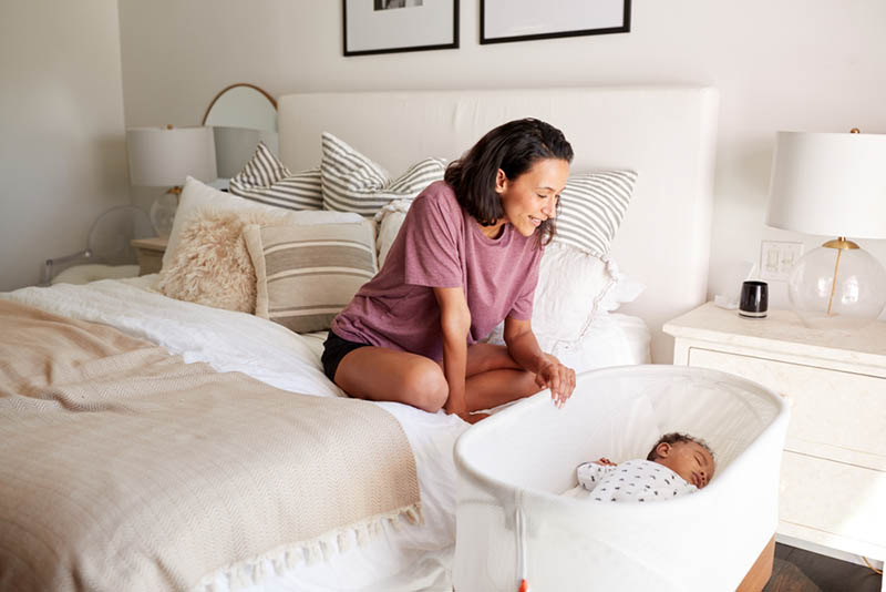Junge Mutter schaut auf ihr Baby in einer Wiege am Bett