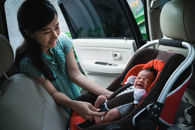 Junge Mutter setzt weinendes Baby im Autositz ins Auto