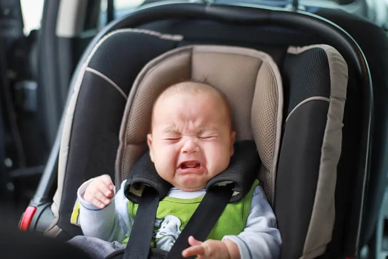 Kleiner Babyjunge weint, während er in einem sicheren Autositz befestigt ist
