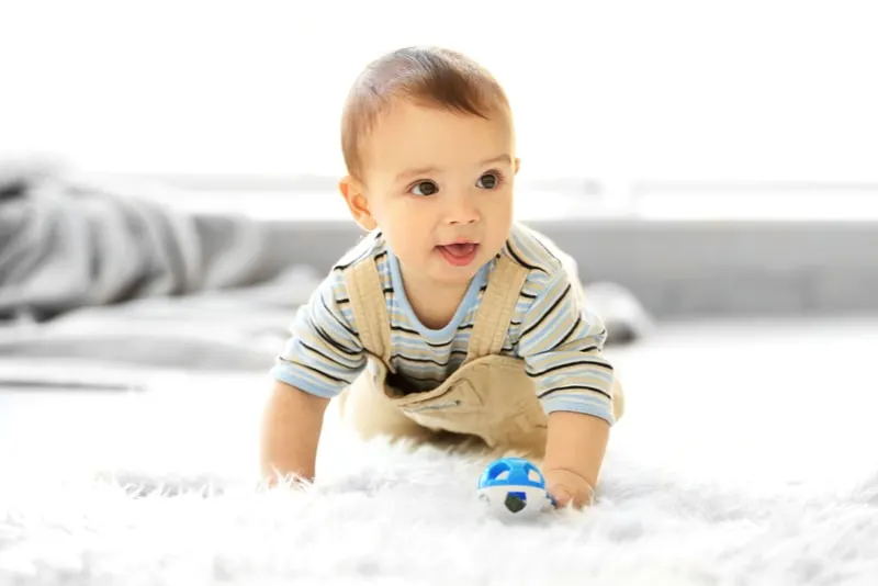 Kleiner Junge mit einem Spielzeug, das zu Hause auf dem Boden kriecht