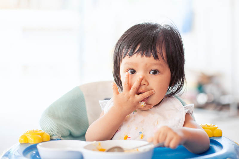 Kleines Mädchen isst in einem Hochstuhl