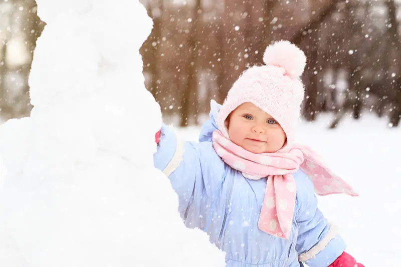 Kleines Mädchen spielt mit Schnee im Freien