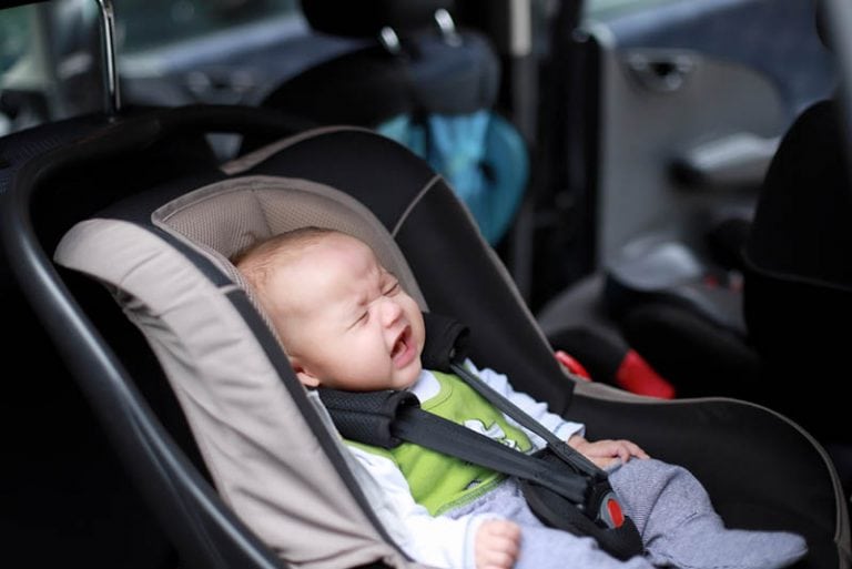 kleines weinendes Baby in einem Autositz mit angelegtem Sicherheitsgurt