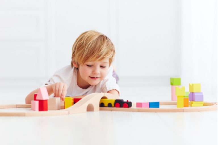 süßes Kind, das mit Spielzeugbahnstraße zu Hause spielt