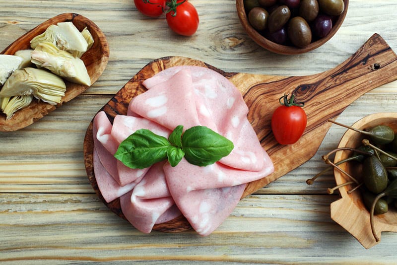 Mortadella-Salami in Scheiben geschnitten mit Tomaten und anderem Gemüse auf dem Brett