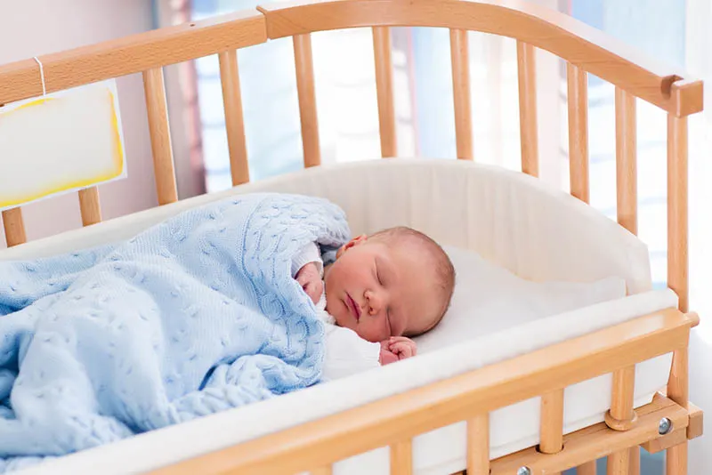 Neugeborenes Baby schläft in einem extra Babybett mit blauer Decke