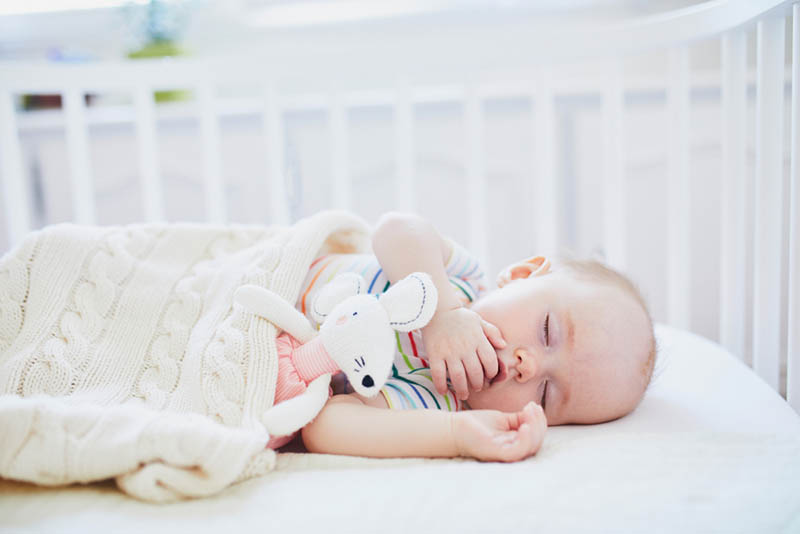 Niedliches Baby schläft mit Kaninchenspielzeug im Babybett