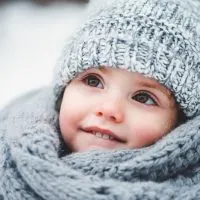 kleines Mädchen steht im Schnee und trägt eine Wintermütze und Schal