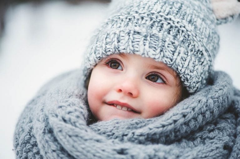 kleines Mädchen steht im Schnee und trägt eine Wintermütze und Schal