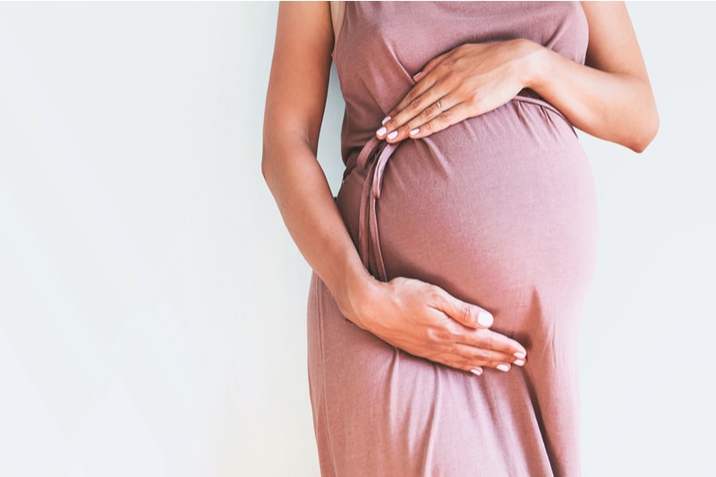 Schwangere Frau im Kleid hält Hände am Bauch