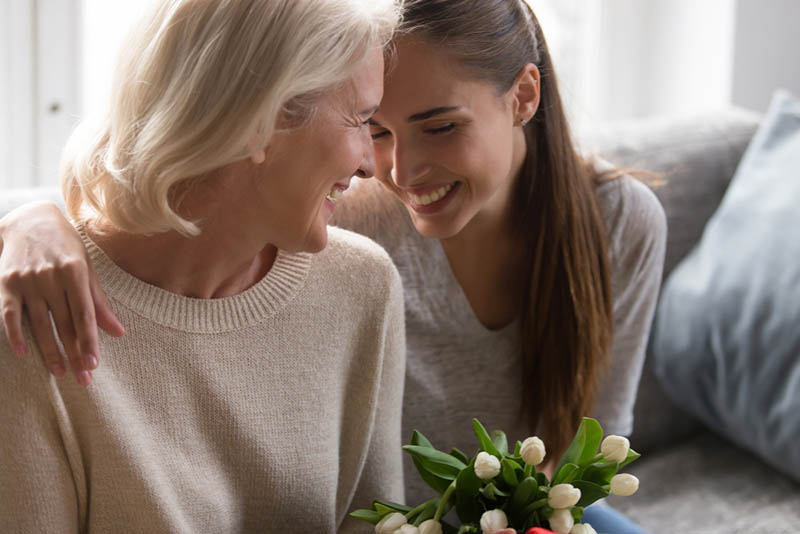 ältere Frau umarmt mit Schwiegertochter geben ihr Blumen