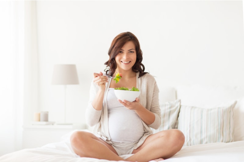 glückliche schwangere Frau, die Gemüsesalat isst