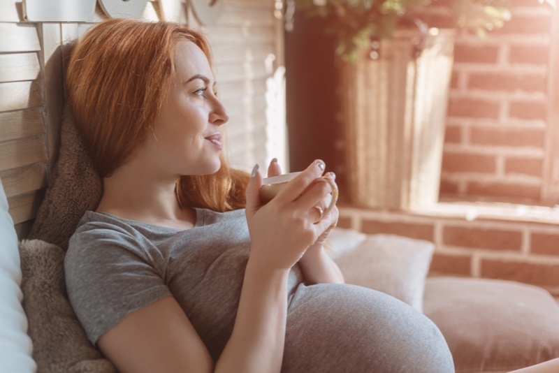 glückliche schwangere Frau mit Tasse, die Tee zu Hause trinkt