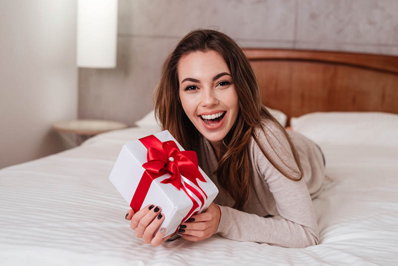 glückliche schöne Frau auf dem Bett liegend mit Geschenk-Box