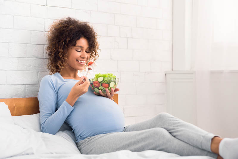 glückliche schwangere Frau essen gesunden Salat auf dem Bett