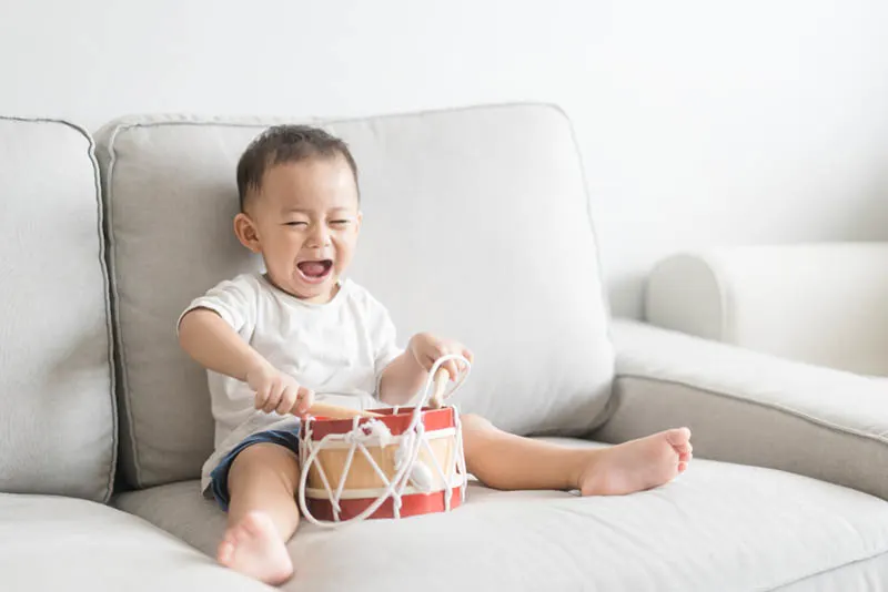 glücklicher kleiner Junge spielt Schlagzeug auf der Couch