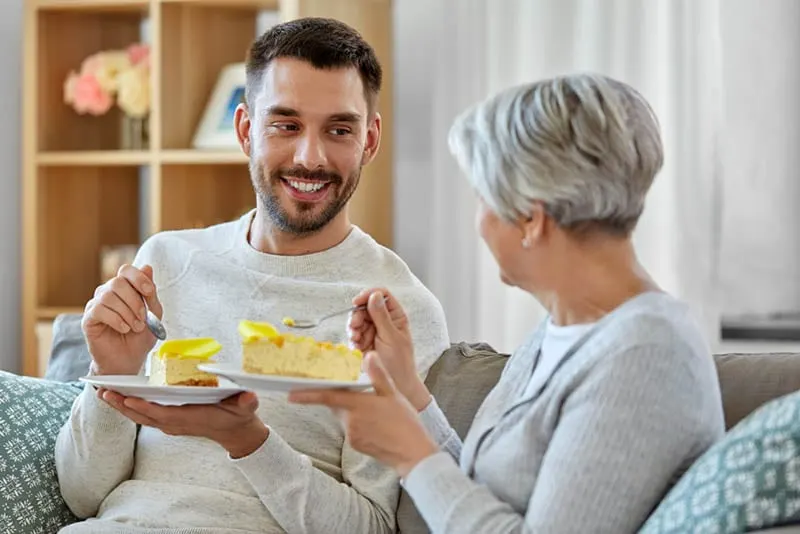 junger Mann isst einen Kuchen mit Schwiegermutter auf der Couch