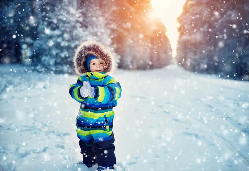 kleiner Junge im Winteranzug spielt auf dem Schnee