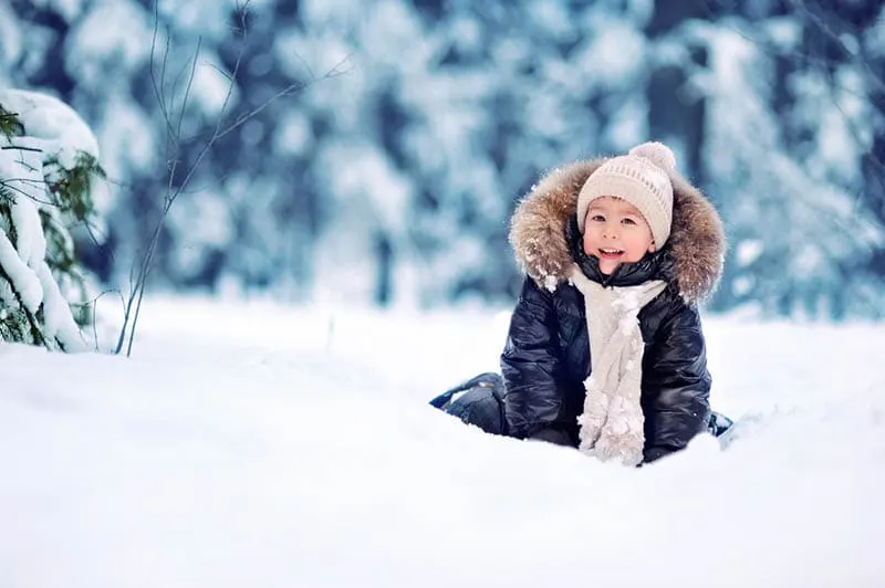 kleiner Junge sitzt im Schnee draußen im Wald