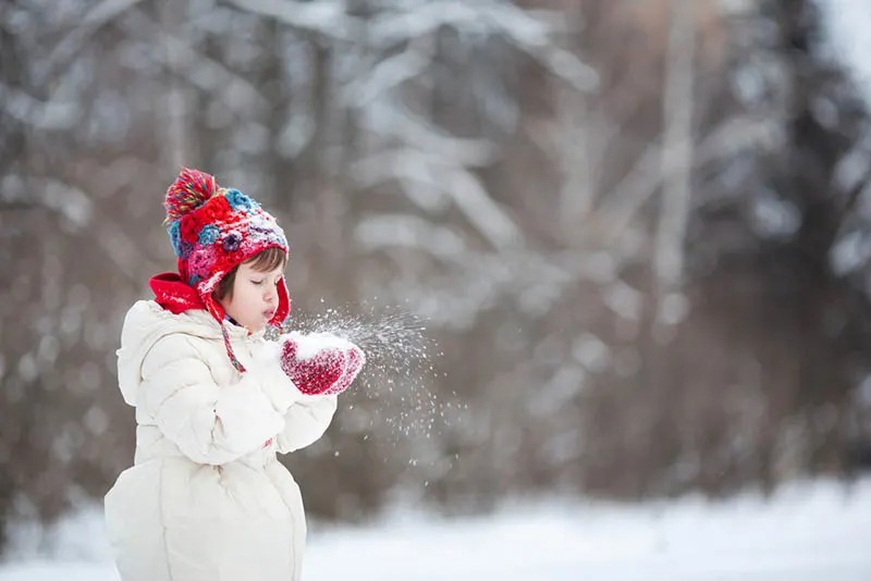 kleines Mädchen bläst den Schnee aus den Händen