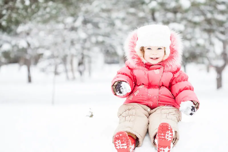 kleines Mädchen hält einen Schneeball draußen im Wald