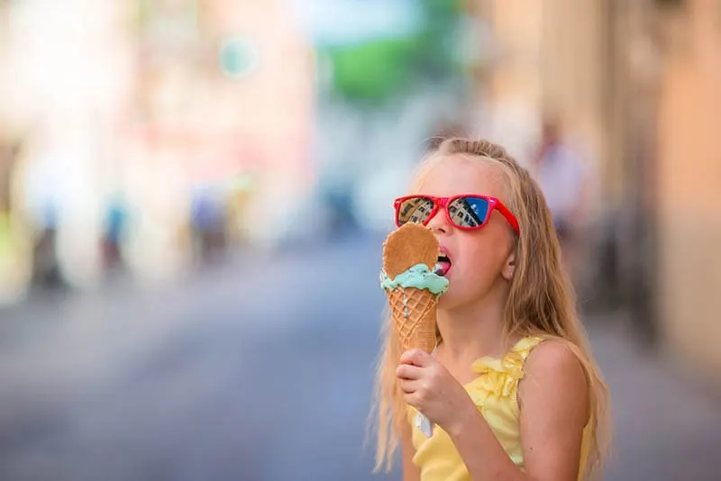 kleines blondes Mädchen isst ein Eis auf der Straße