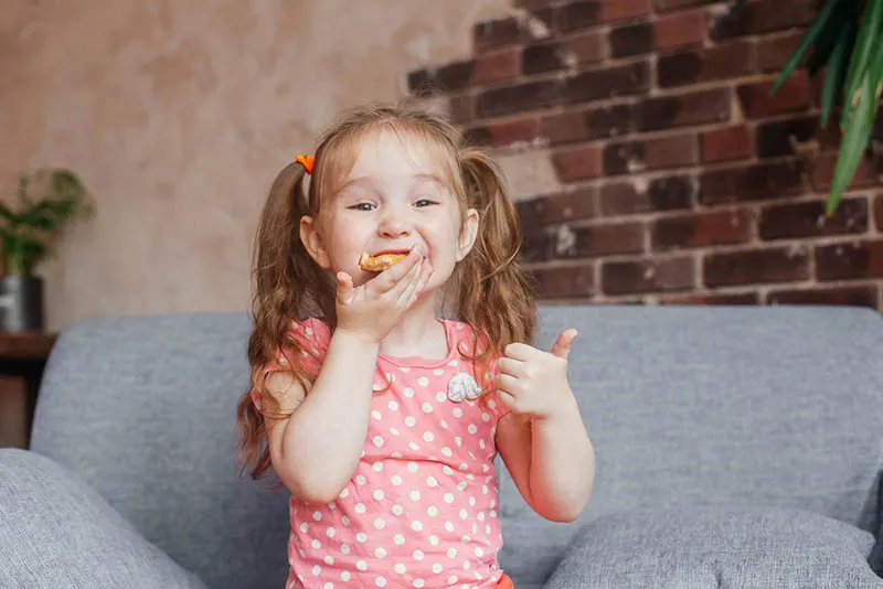 lächelndes kleines Mädchen sitzt auf der Couch und isst Pizza