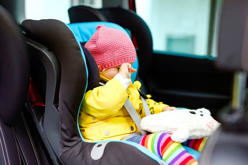 müde Baby Mädchen sitzt in einem Autositz mit Spielzeug