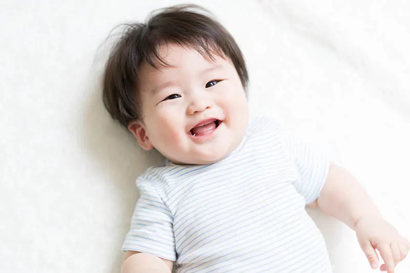 niedliche japanische Baby Junge lächelnd, während auf dem Bett liegend