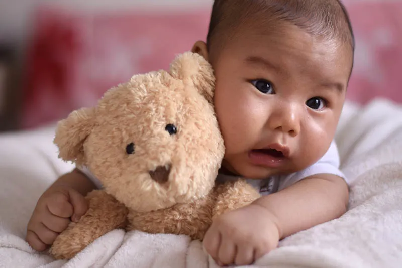 niedlichen Baby Bos auf dem Bett liegend mit Teddybär Spielzeug