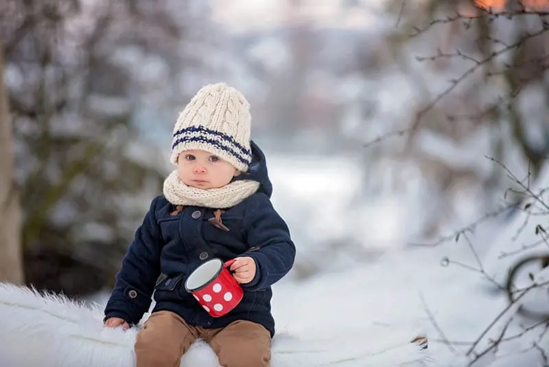 niedlichen Baby Junge hält eine Tasse auf dem Schnee