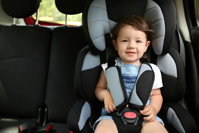 niedlichen Baby Junge sitzt in einem Autositz mit Sicherheitsgurten