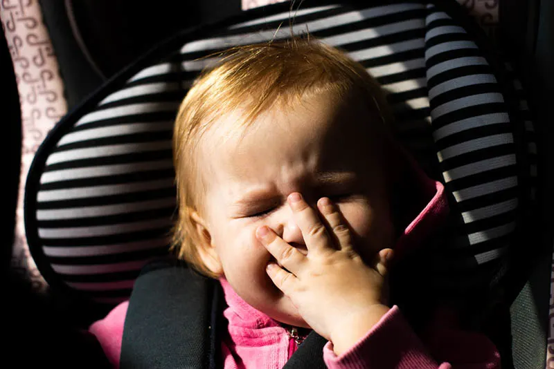 niedlichen Baby Mädchen hält Hand auf Gesicht in den Autositz