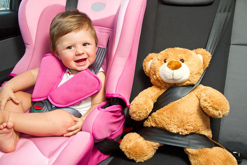 niedlichen Baby Mädchen sitzt in einem rosa Autositz mit Teddybär Spielzeug