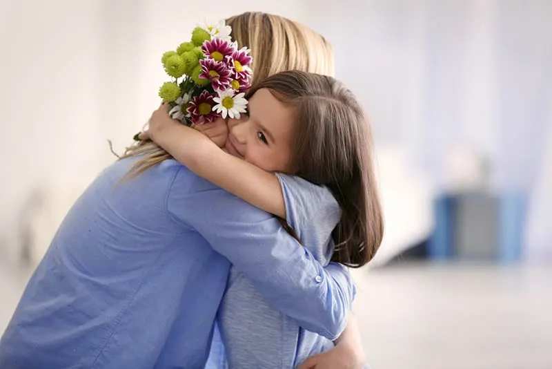 niedlichen kleinen Mädchen umarmt Mutter und geben ihr Blumen