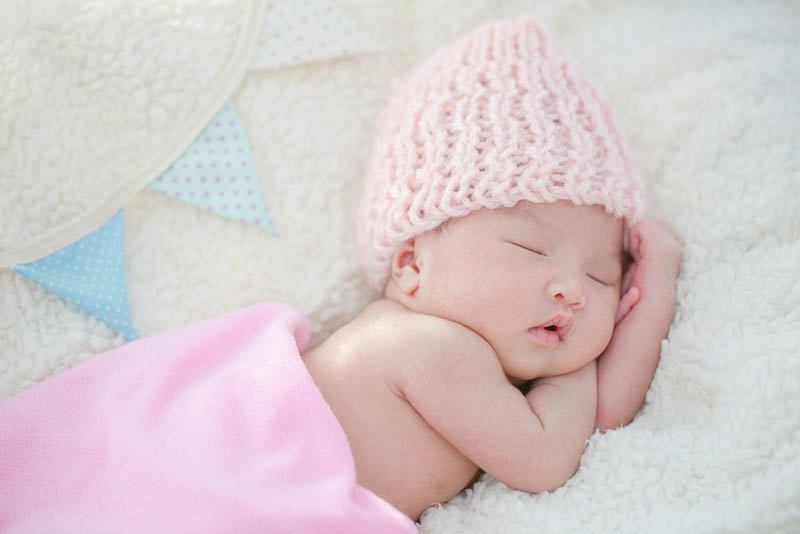 niedlichen neugeborenen Baby mit rosa Hut schlafen auf dem Bett