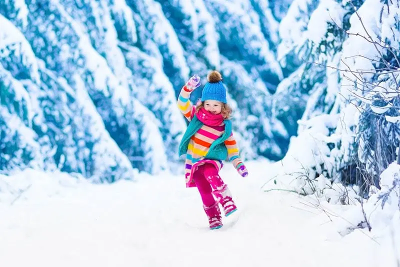 süße lächelnde Mädchen trägt bunte Kleidung auf Schnee