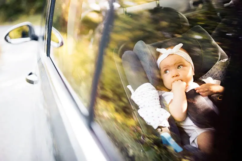 süßes Baby Mädchen mit Stirnband fahren im Auto, während in Baby-Sitz sitzen