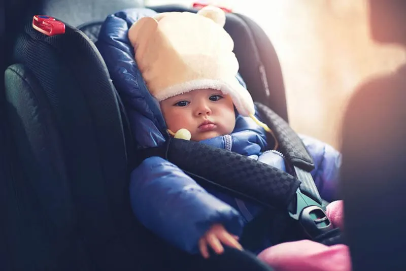 süßes Baby in Winterkleidung in einem Autositz sitzend