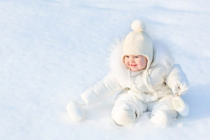 süßes Baby in weißen Winteranzug sitzt auf dem Schnee