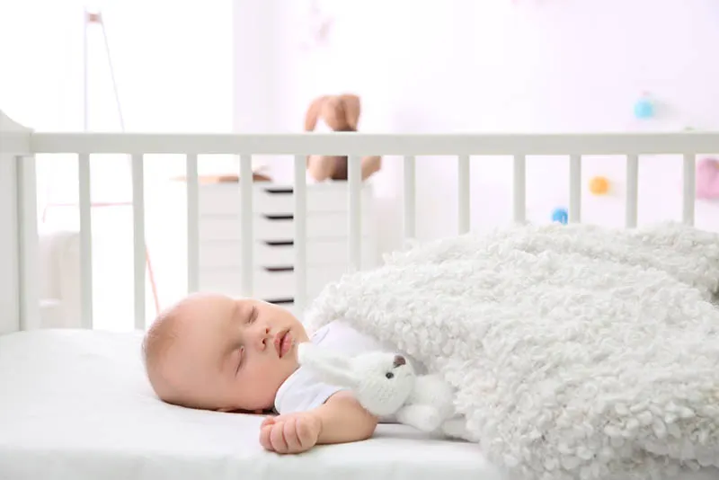 süßes Baby schlafend in einer Wiege mit weißer Decke bedeckt