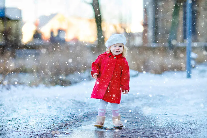 süßes kleines Mädchen in rotem Mantel stehend im Schnee
