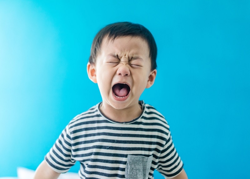 wütend Kleinkind weint und schreit vor einem blauen Hintergrund
