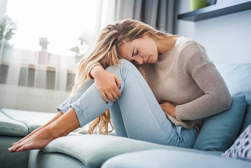 Frau mit Unterleibsschmerzen beim Sitzen auf dem Sofa 