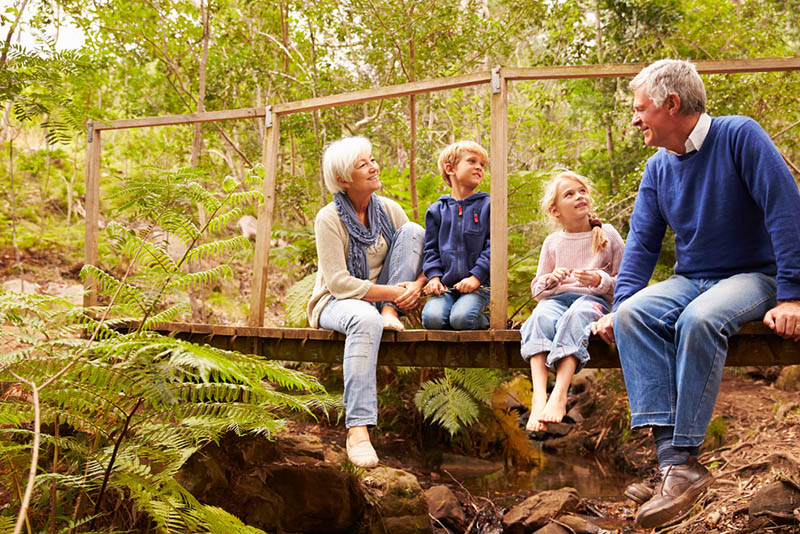 Großeltern sitzen mit Enkelkindern auf einer Brücke in einem Wald
