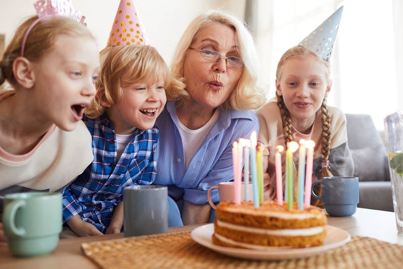 Großmutter bläst Kerzen auf dem Kuchen zusammen mit Enkelkindern