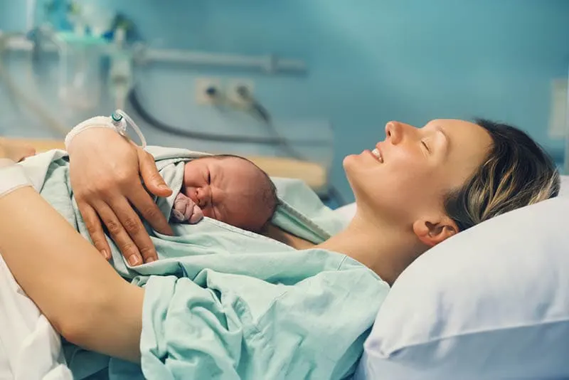 Junge Mutter umarmt ihr neugeborenes Baby nach der Geburt